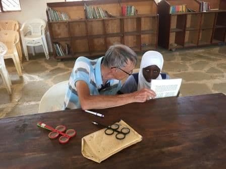A visitor testing a woman's reading vision with a chart at a library table
