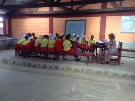 Secondary schoolgirls in yellow and red uniform seated at benches for a sewing lesson