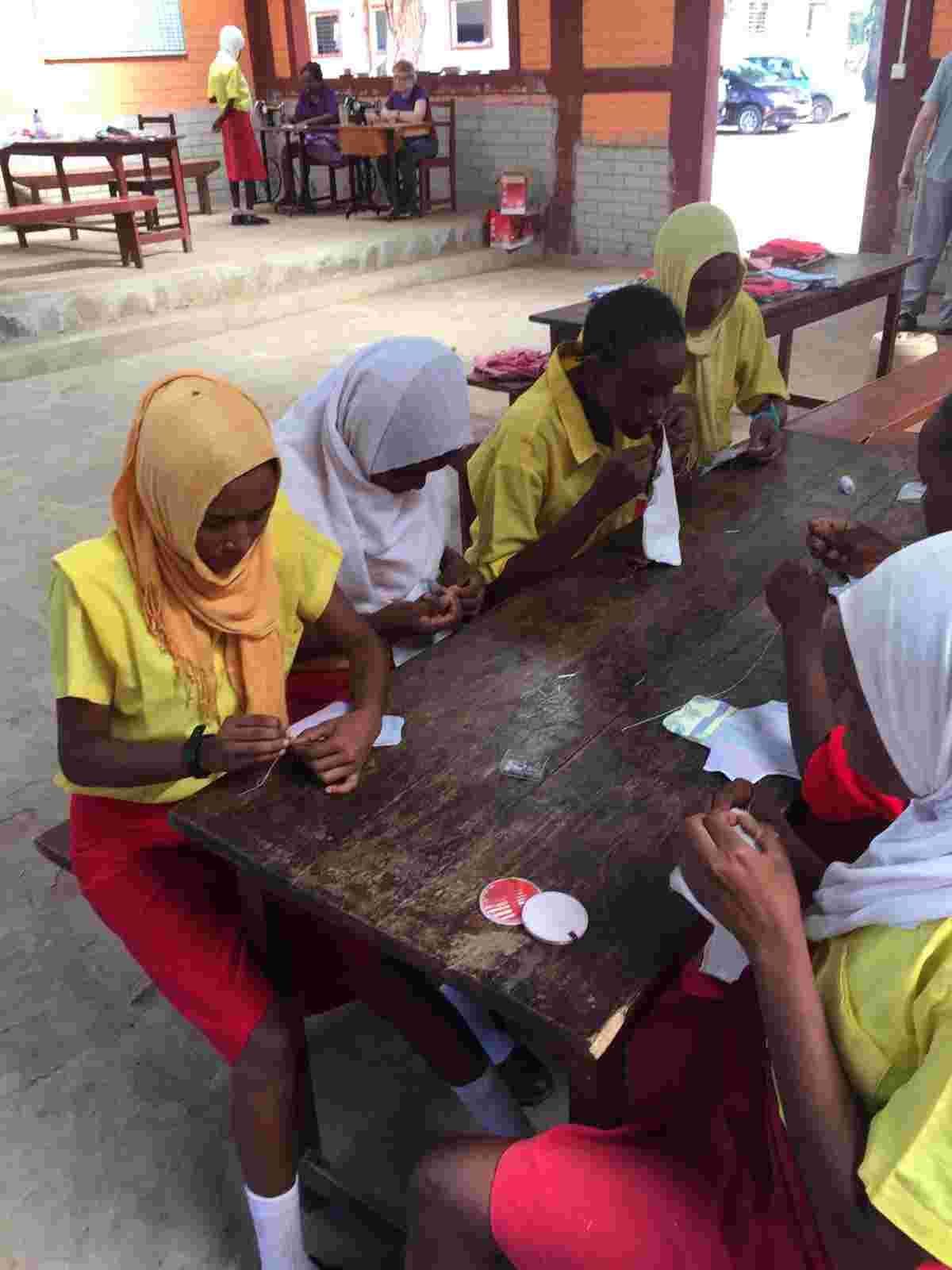 Schoolgirls sewing sanitary pads at a long table