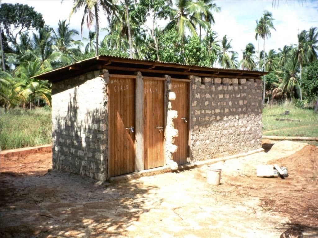 A small toilet block with wooden doors built of coral stone among palm trees