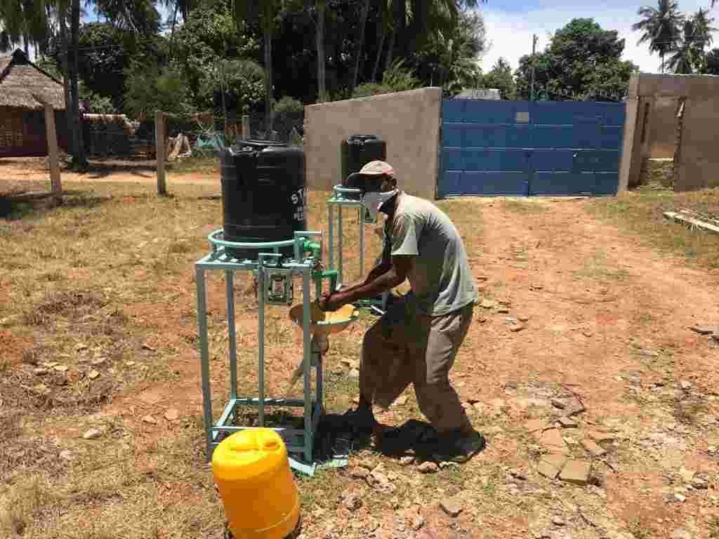 A man setting up a foot-operated handwashing station near the school gate