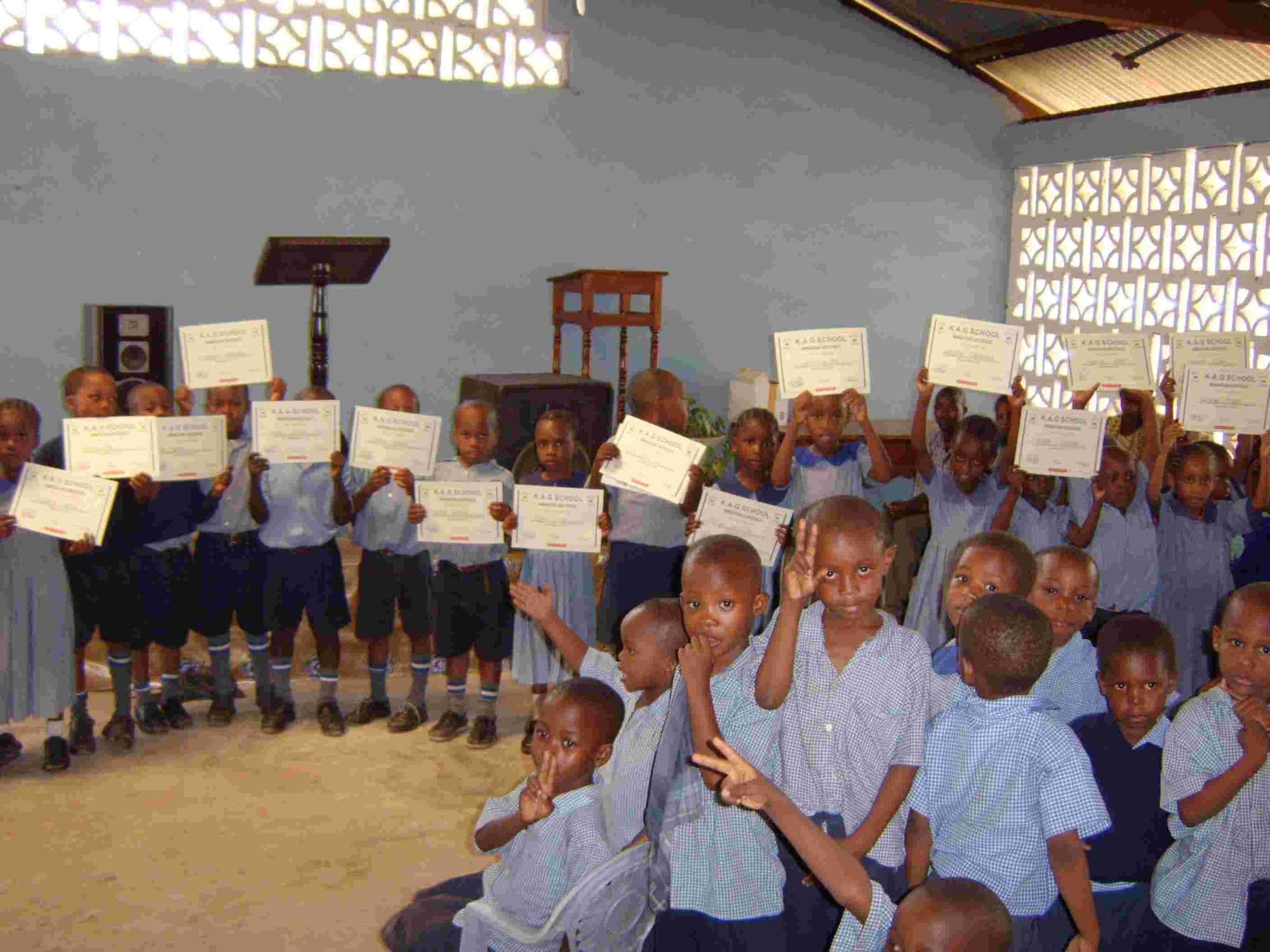 Pupils in blue uniform holding up certificates at graduation