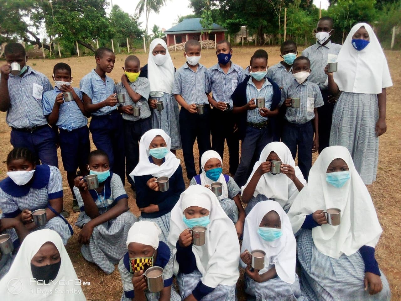 Masked pupils sitting outside drinking porridge from metal cups