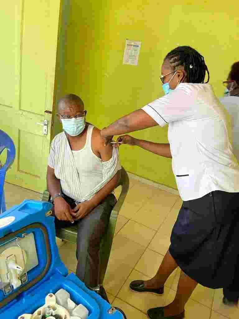 A health worker in a mask vaccinating a seated man in the arm