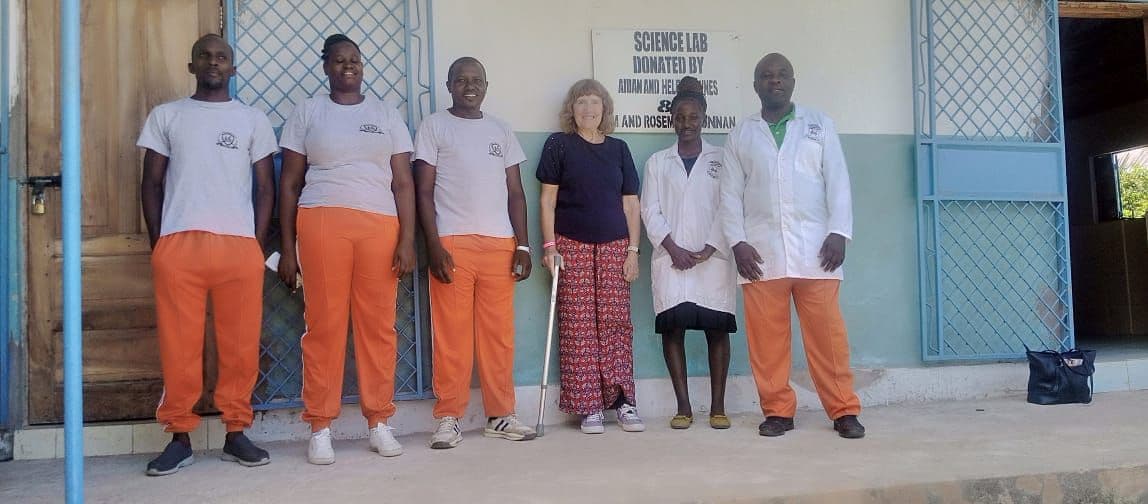 Junior High teachers in lab coats and orange trousers standing with a visitor outside the lab