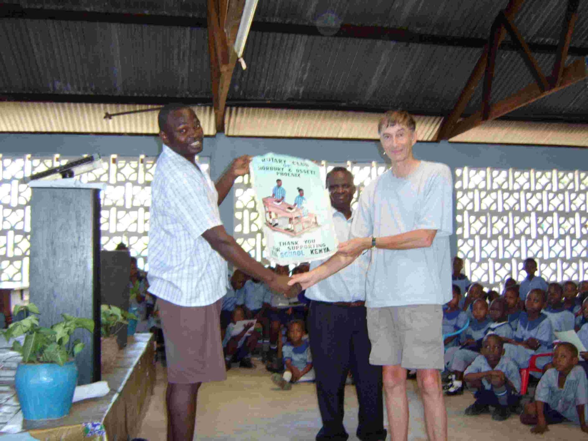 Two men presenting a poster at the front of a hall full of pupils