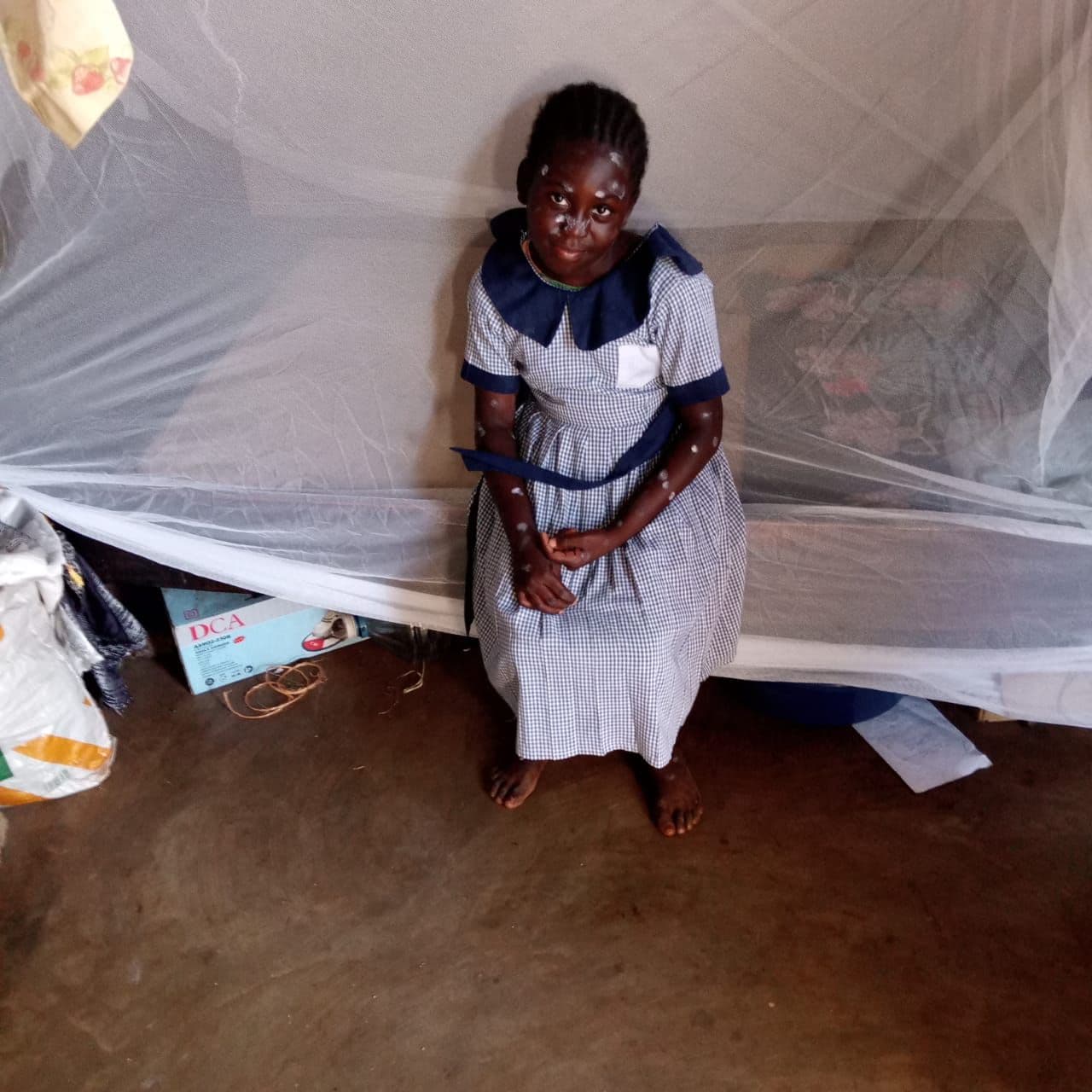A schoolgirl sitting under a new mosquito net in her home