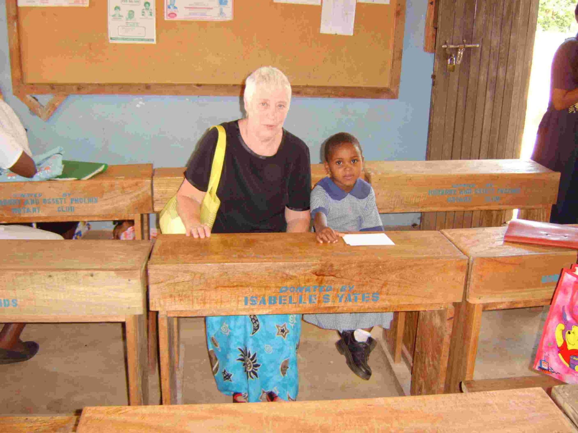 A visitor sitting at a school desk next to a young pupil