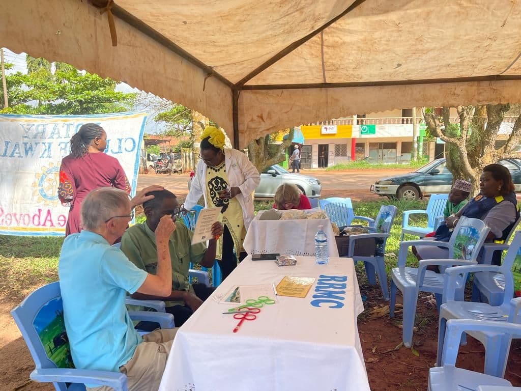 A visitor fitting lenses to test a man's eyes under a marquee at the eye camp
