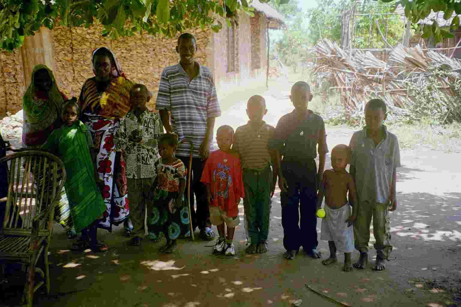 A local family with many children standing outside their mud and thatch home