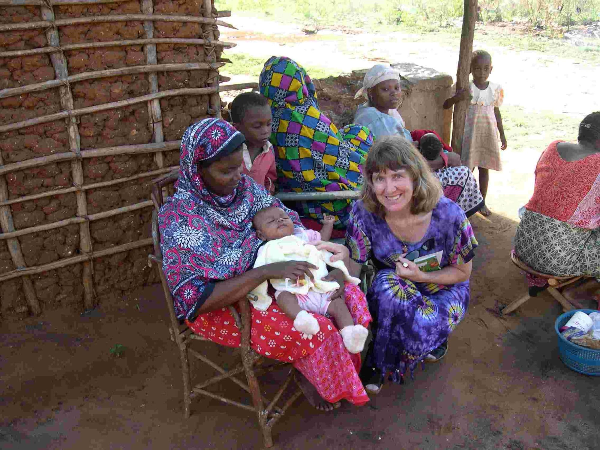 A woman sitting with a mother and her newborn baby outside a mud house