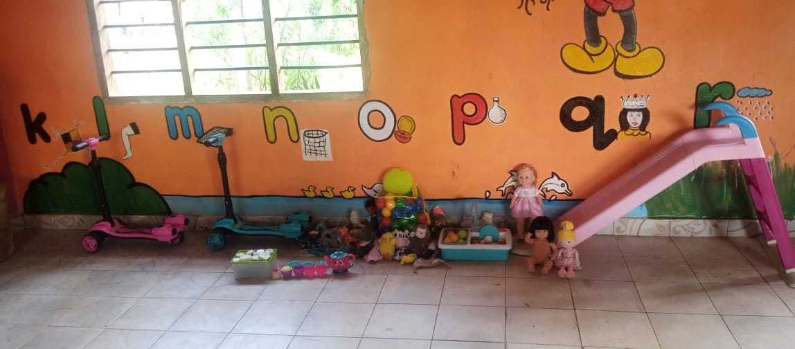 A toy slide, scooters and toys in front of alphabet letters painted on the classroom wall