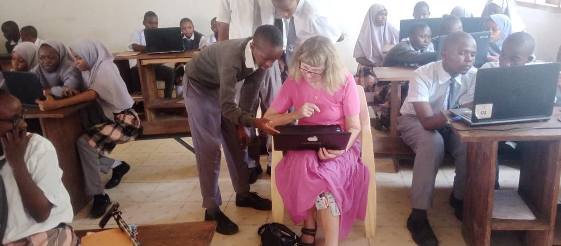A visitor working with pupils on laptops in a classroom