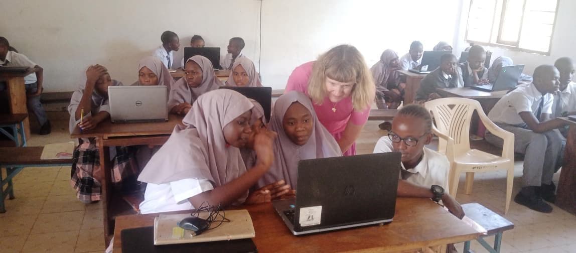 A visitor helping Junior High girls with a laptop at their desk