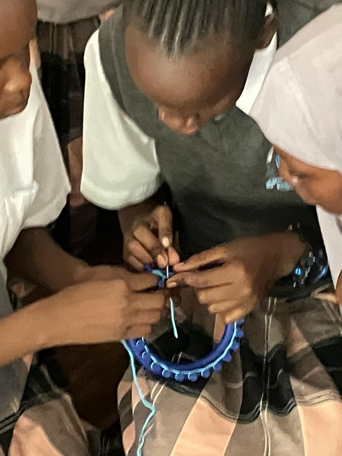 A pupil's hands loom knitting with blue wool