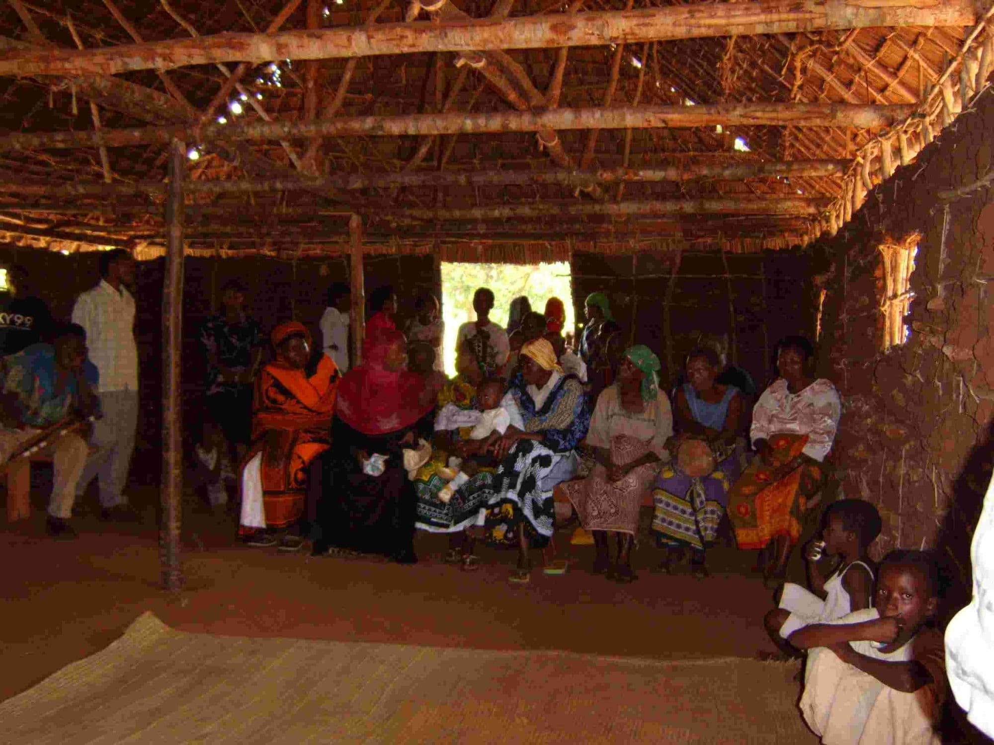 Members of the leprosy community seated in a large thatched hall