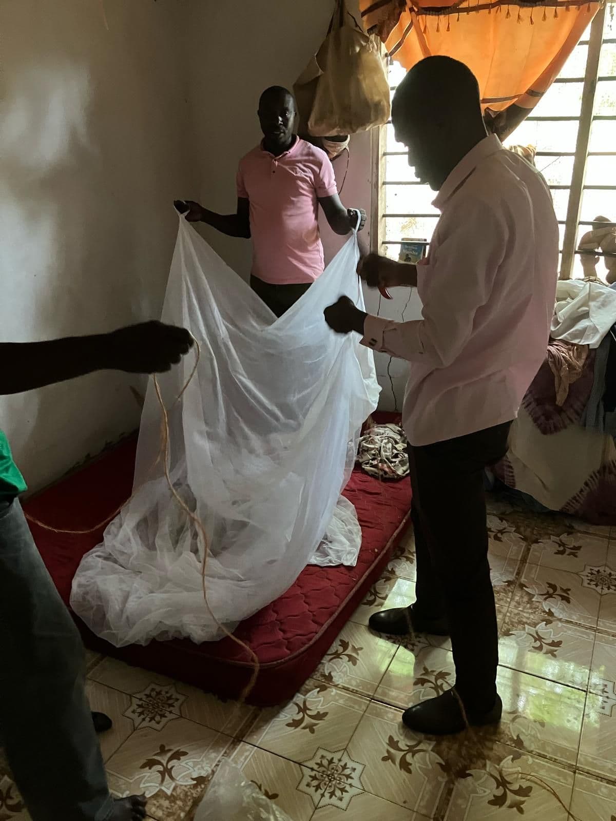 Two men unfolding a mosquito net over a mattress in a home