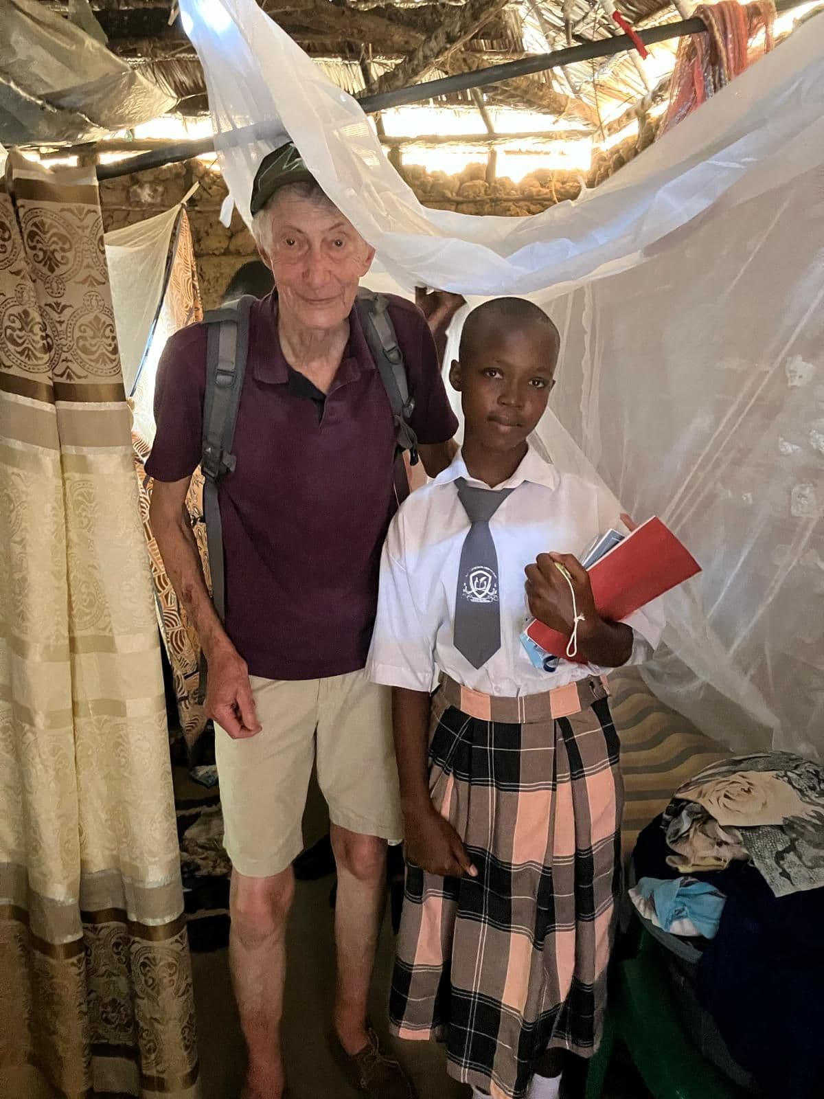 A visitor standing with a schoolgirl holding a red card under a mosquito net