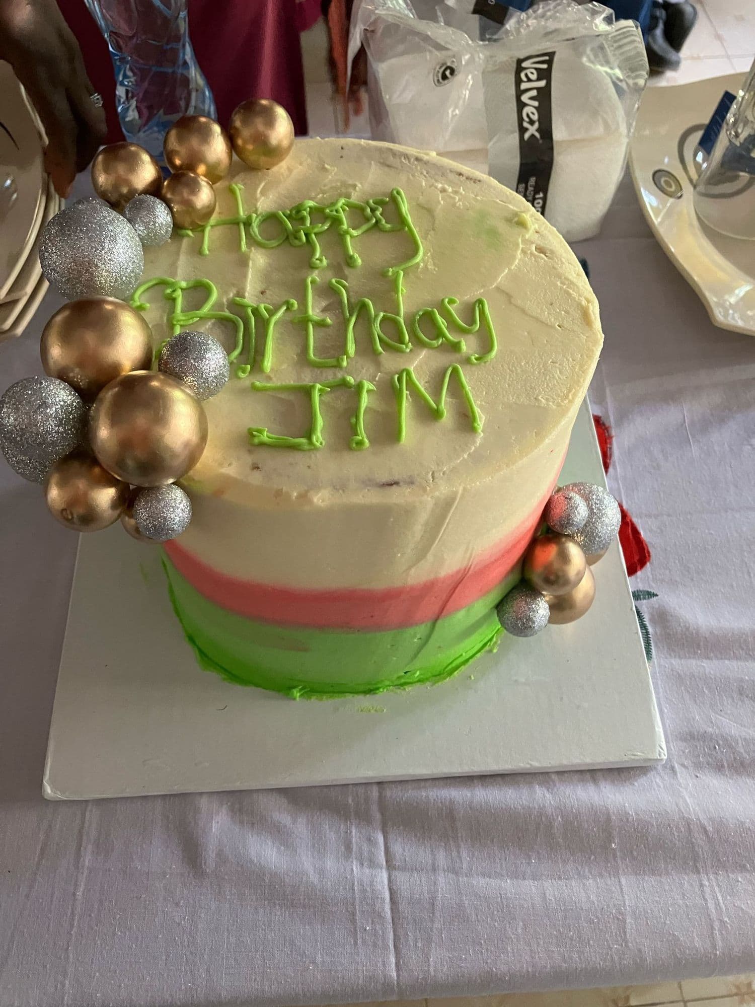 A birthday cake iced Happy Birthday Jim with gold and silver baubles