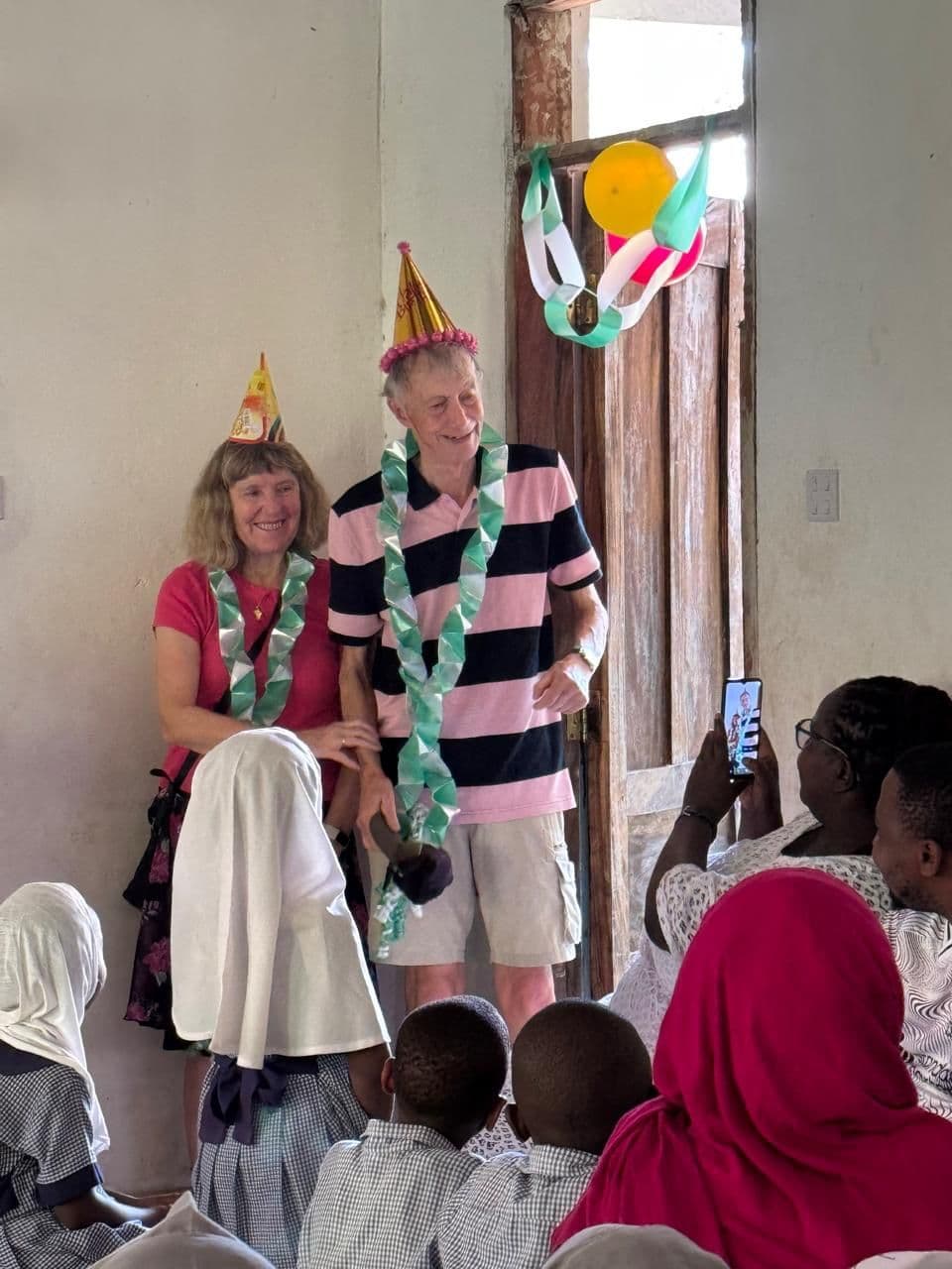 Two visitors in party hats and paper garlands among pupils at the birthday party