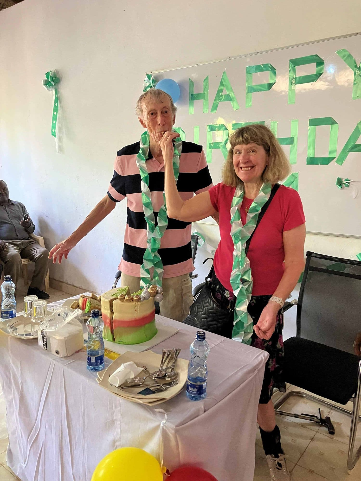 Two visitors in garlands beside the birthday cake on a table