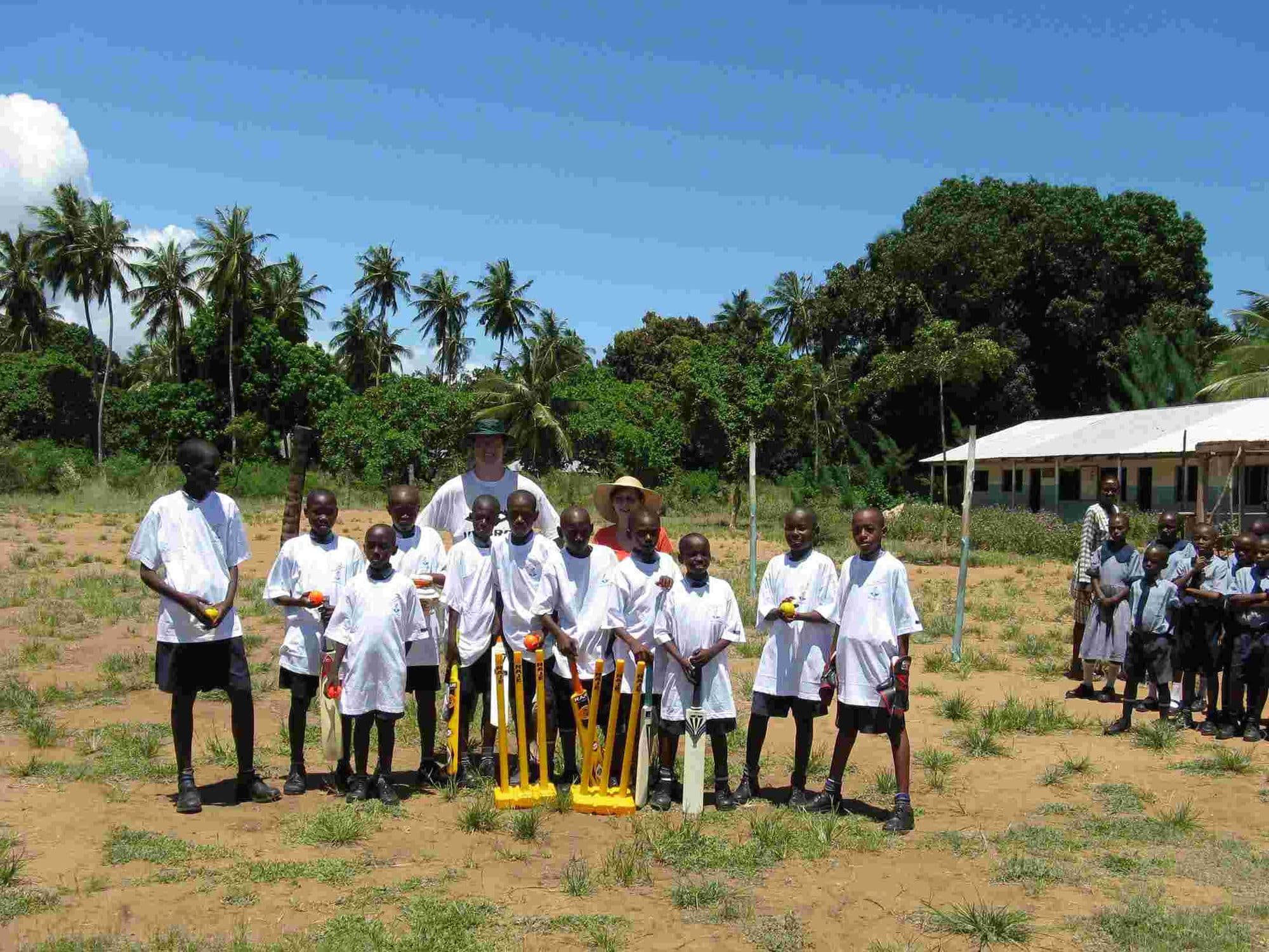 A cricket team of pupils in white shirts posing with bats and stumps on the school field