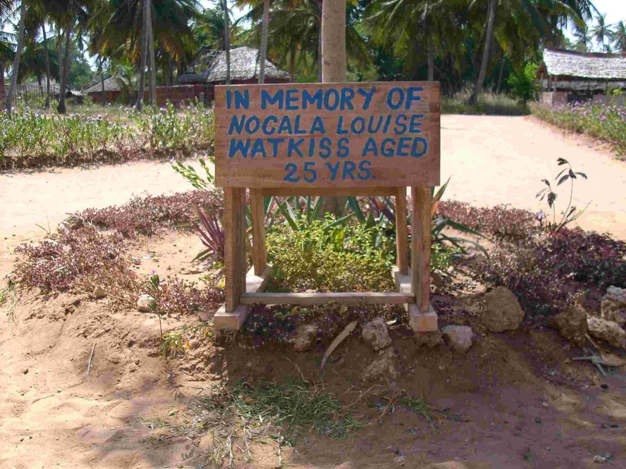 A wooden sign in a garden bed reading In memory of Nicola Louise Watkiss aged 25 yrs