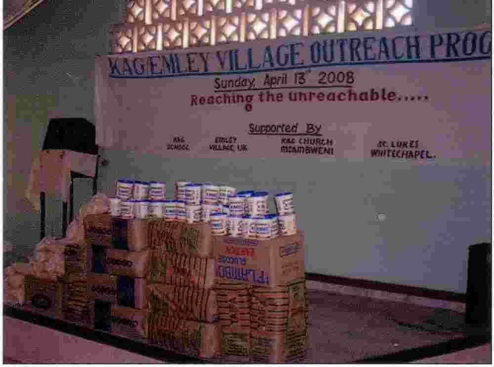 Sacks and boxes of food stacked under a banner for the KAG/Emley Village Outreach Programme, April 2008
