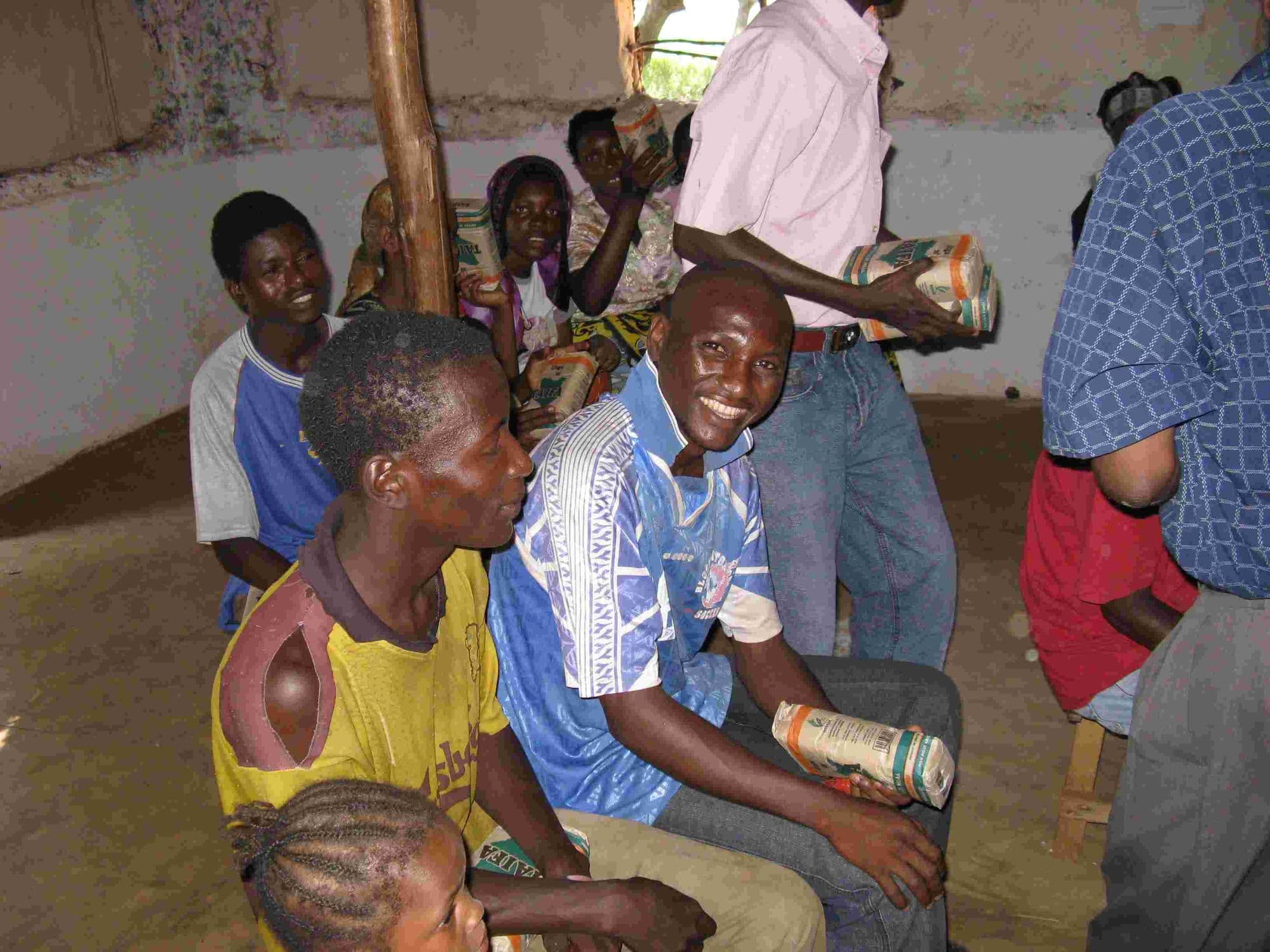 Smiling men from the leprosy community holding food packets