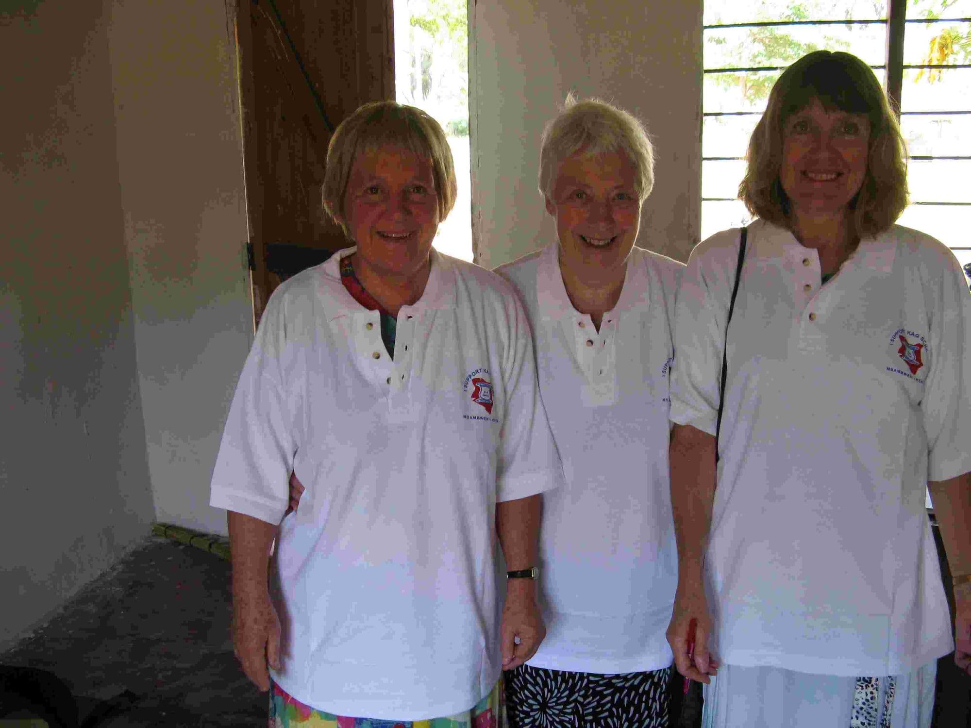 Three visitors in matching white school-logo T-shirts standing in a classroom