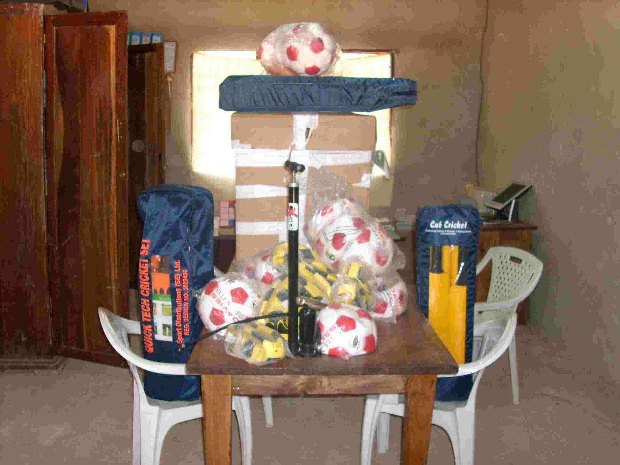 Football boots, footballs, cricket bats and a pump laid out on a table