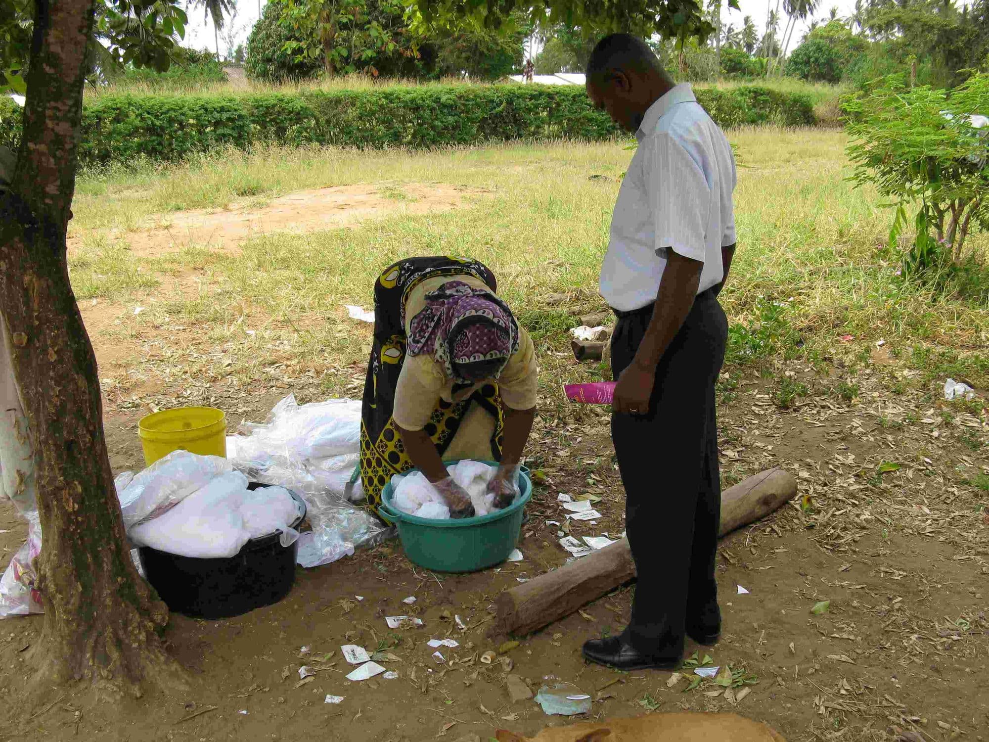 A woman washing new mosquito nets in a basin outdoors while a man looks on