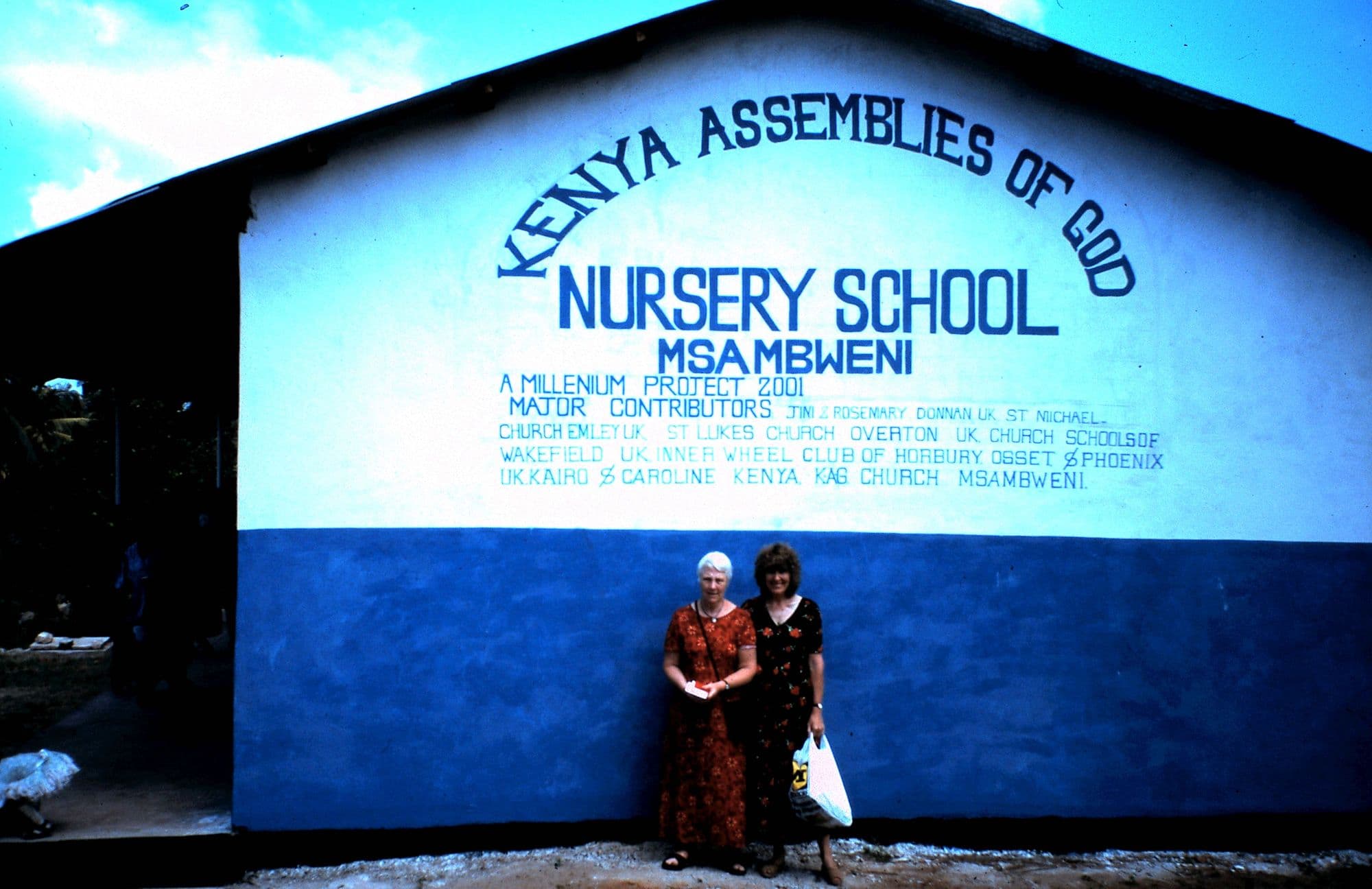 Two women outside the blue and white Kenya Assemblies of God Nursery School, Msambweni