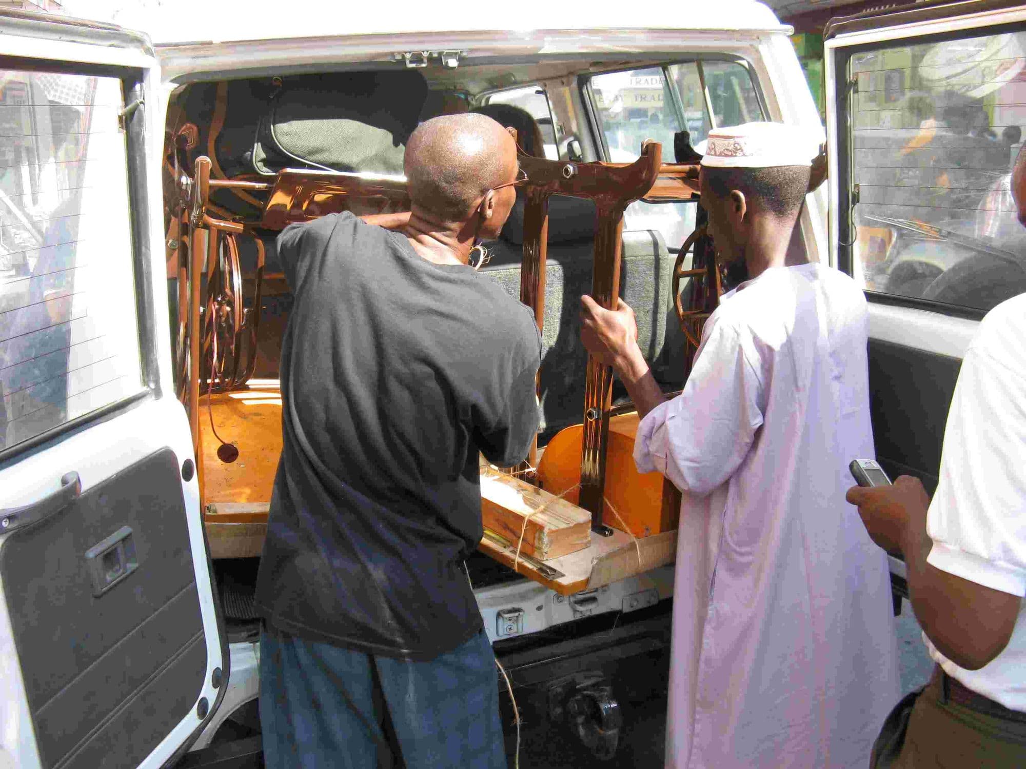 A treadle sewing machine being lifted out of the back of a vehicle