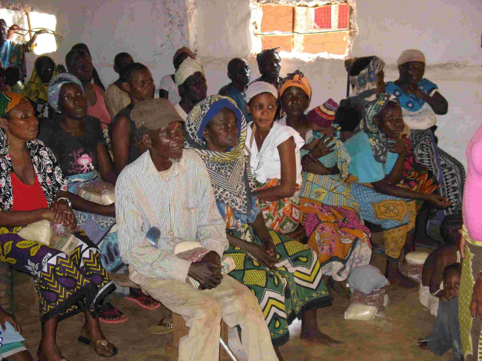Elderly men and women seated together in a crowded room for a food distribution