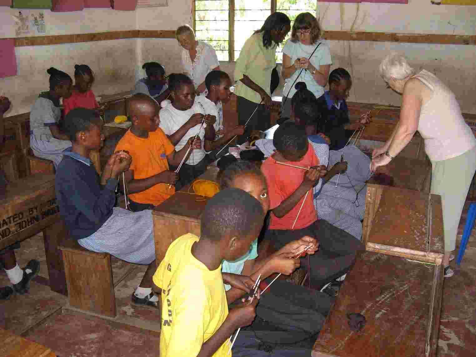 Pupils knitting with sticks at their desks while a visitor helps
