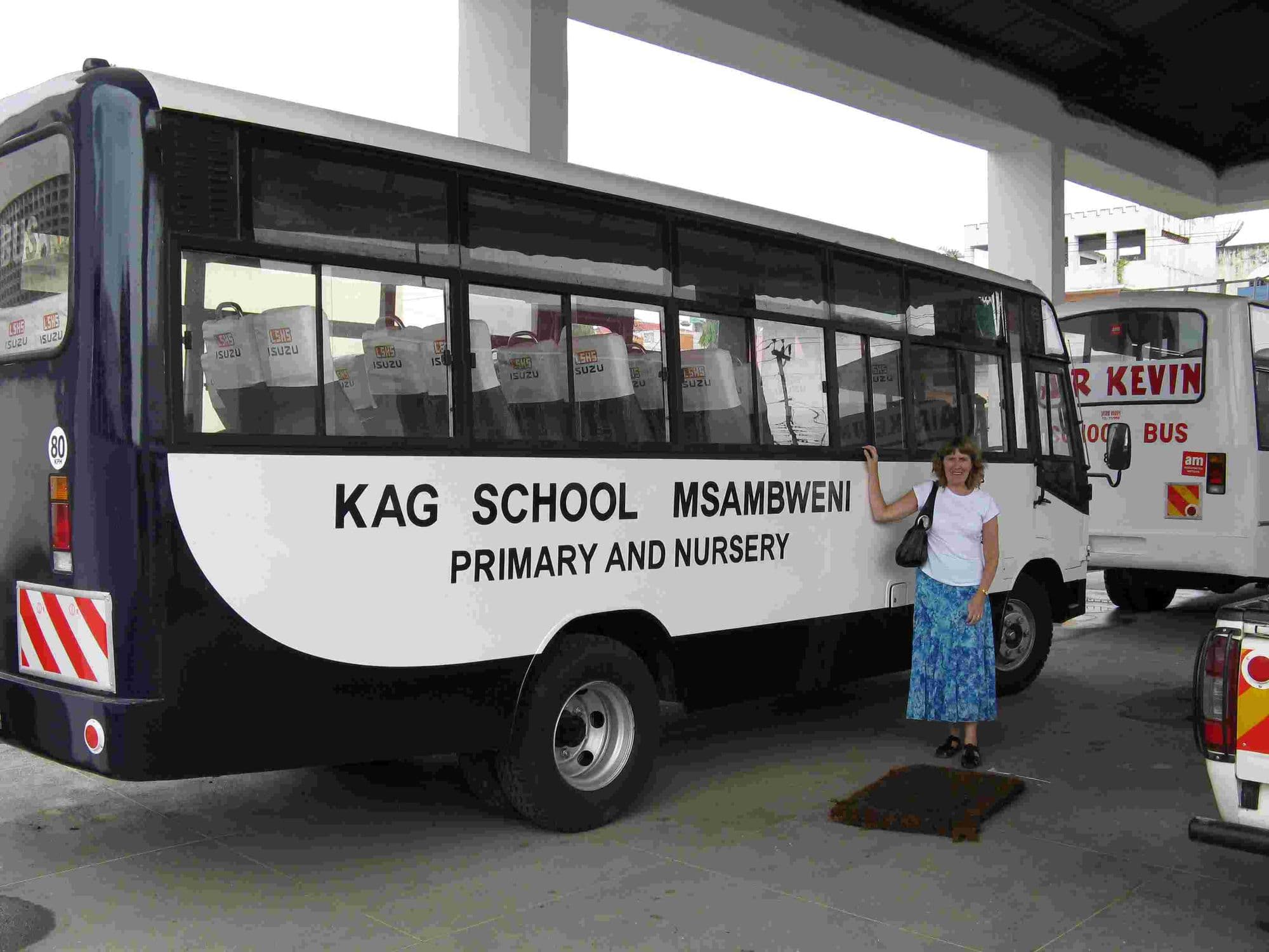A visitor beside the white KAG School Msambweni Primary and Nursery minibus