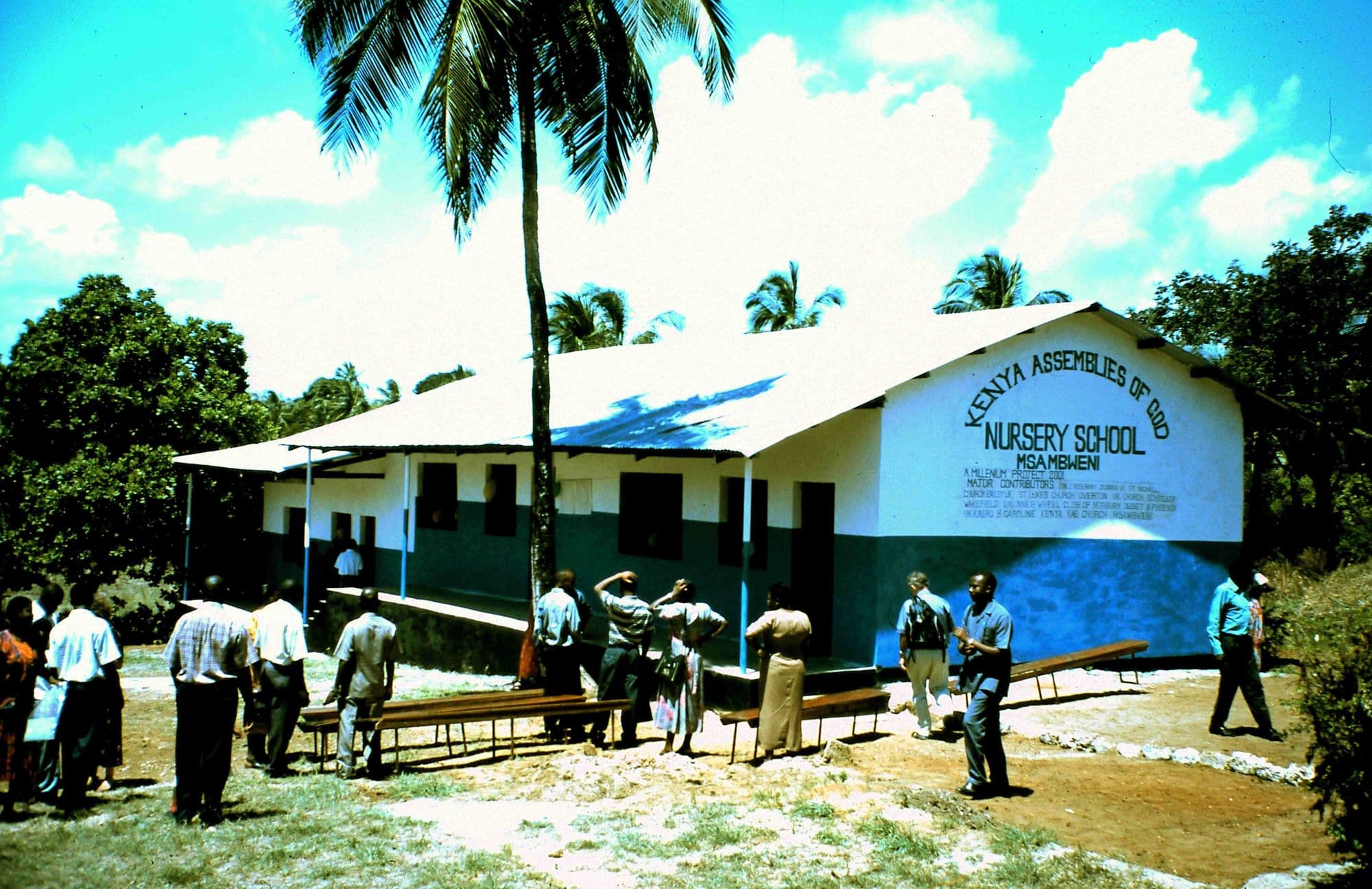 The new nursery school building with its painted sign, people gathered in the yard in front
