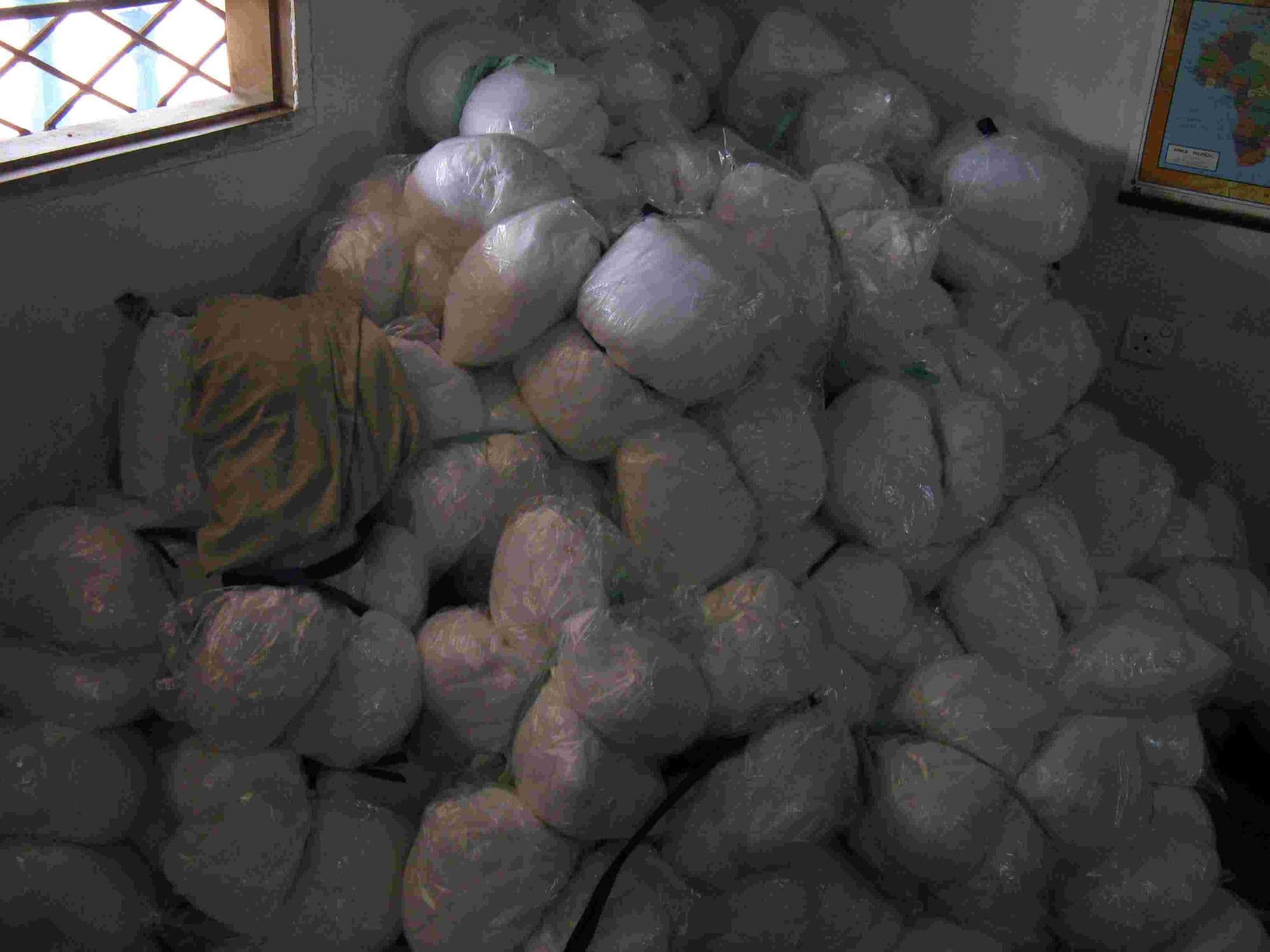 A heap of mosquito nets in plastic packets on a classroom floor