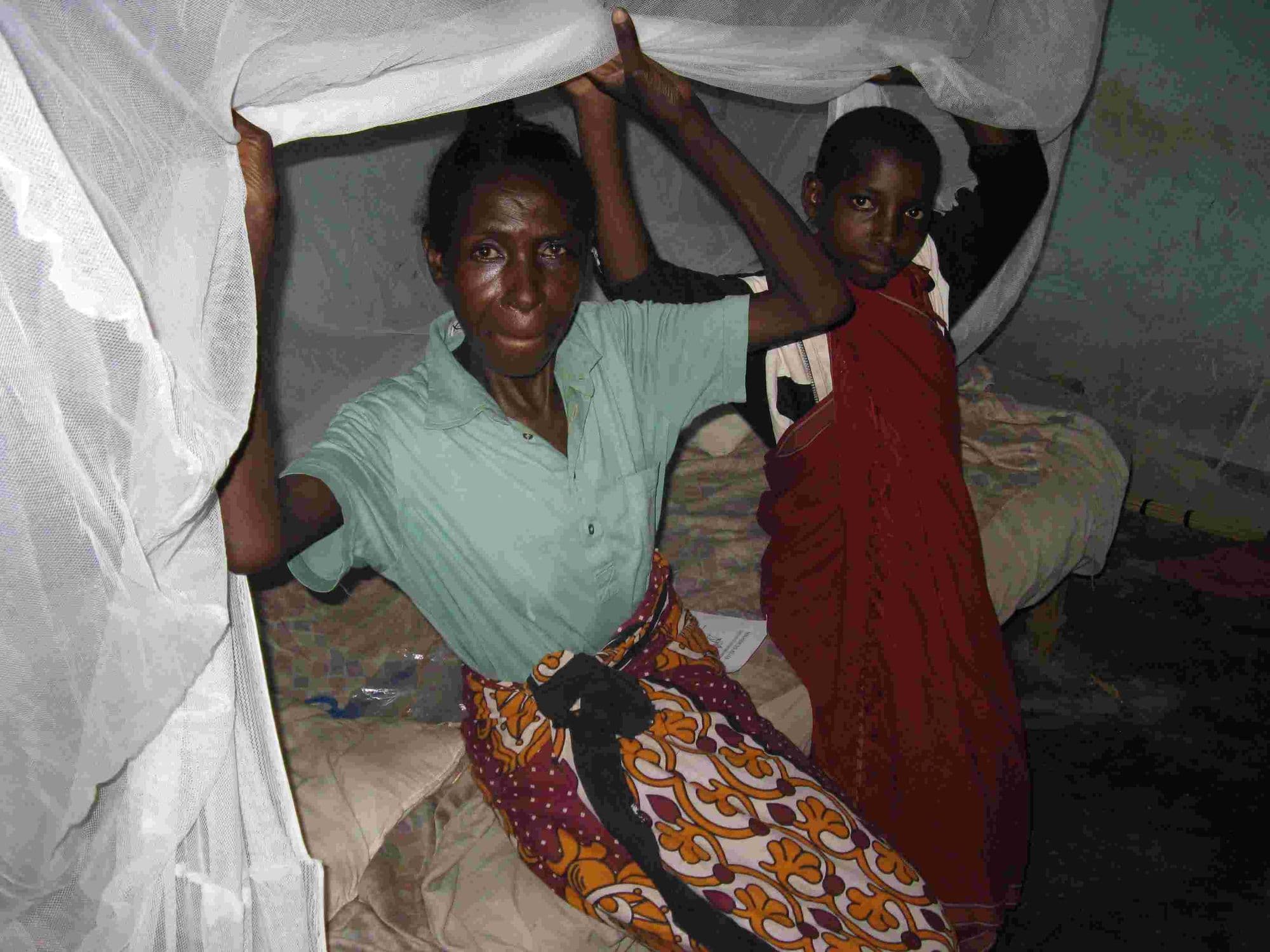 A mother and child sitting under a newly hung mosquito net