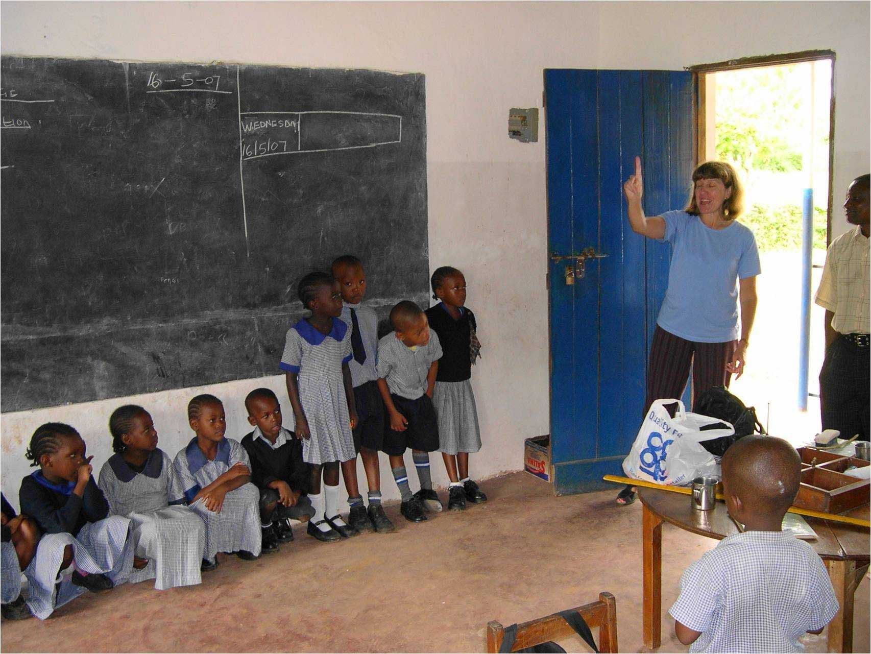 A teacher leading a song with young pupils sitting and standing along a classroom wall