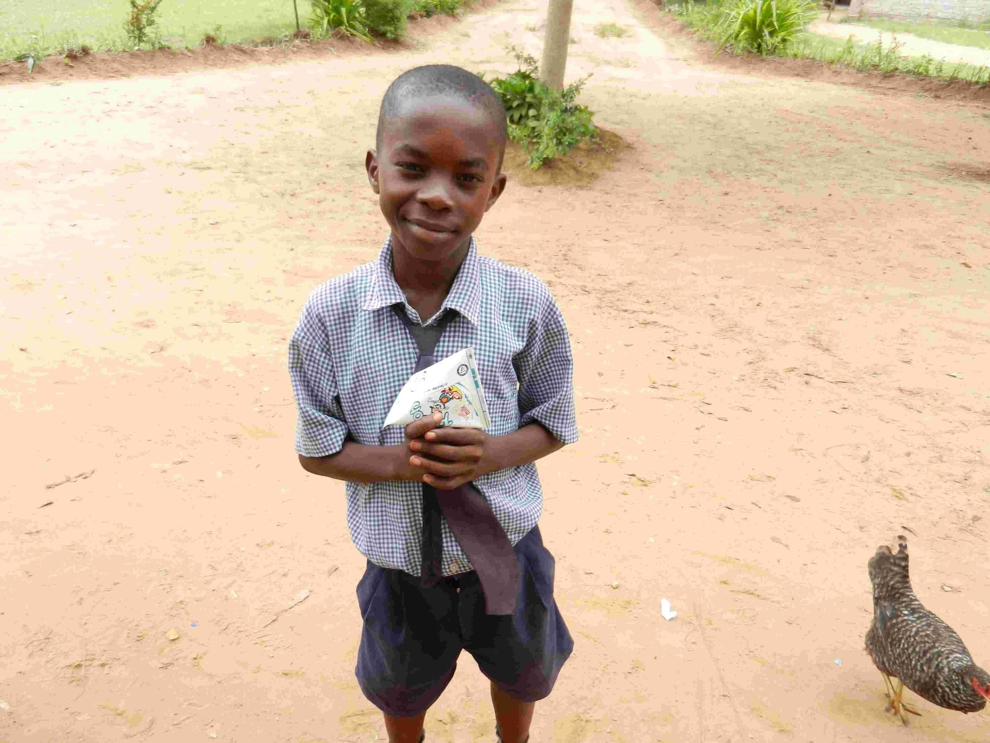 A young pupil holding a packet of milk outdoors