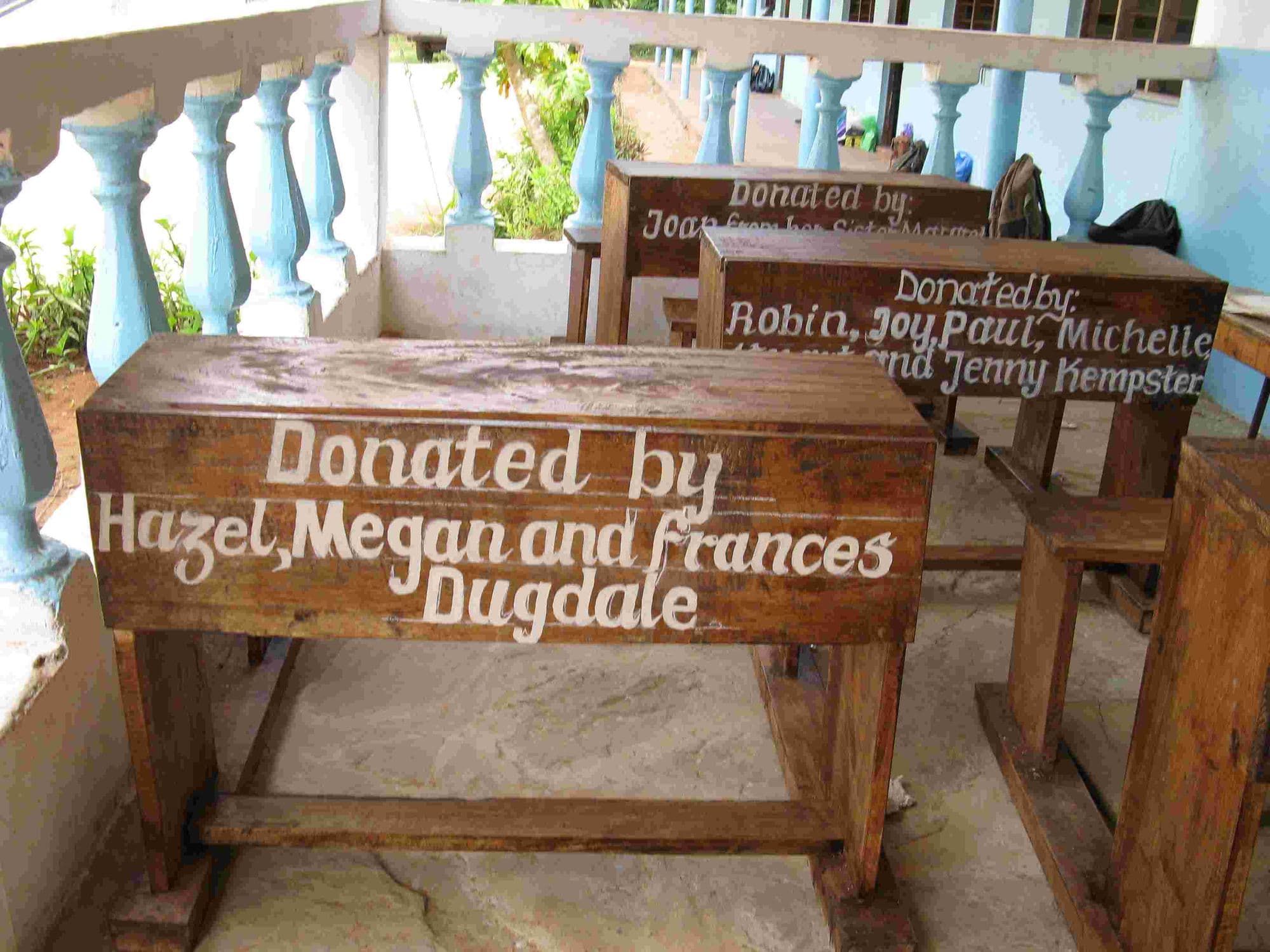 Wooden desks with painted donor names on the classroom verandah
