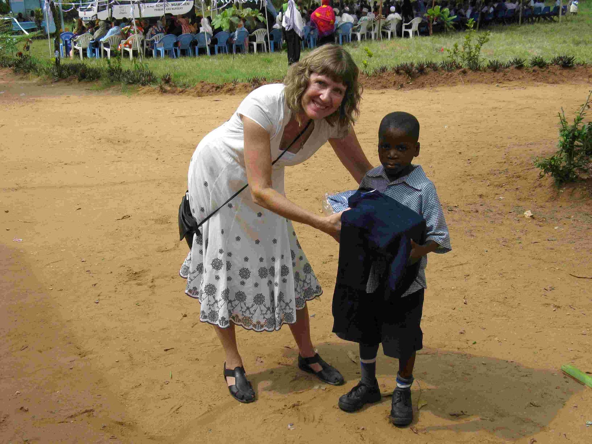 A visitor helping a boy try on a new school uniform outdoors