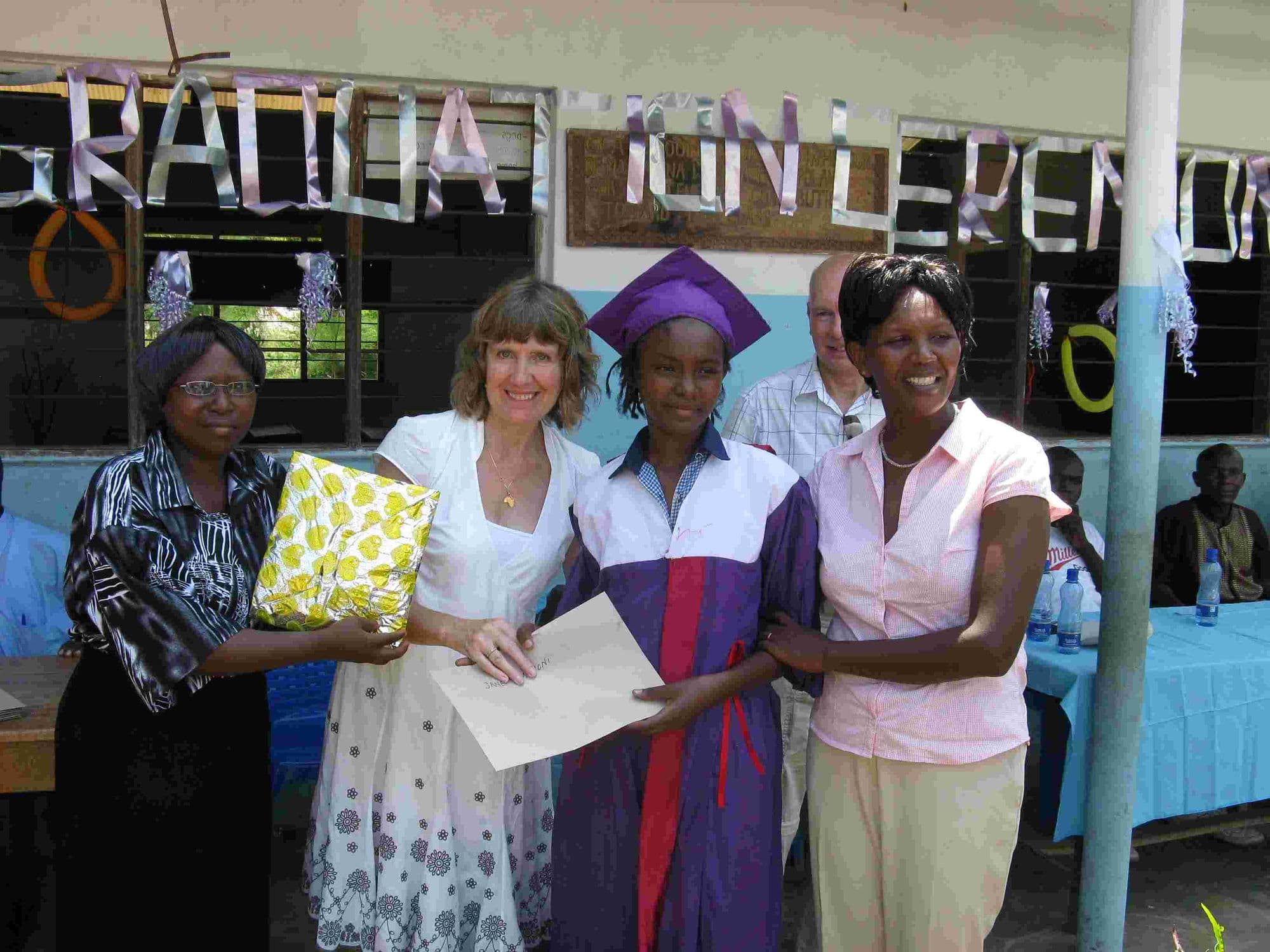A graduate in a purple gown receiving a certificate and gift from visitors and teachers