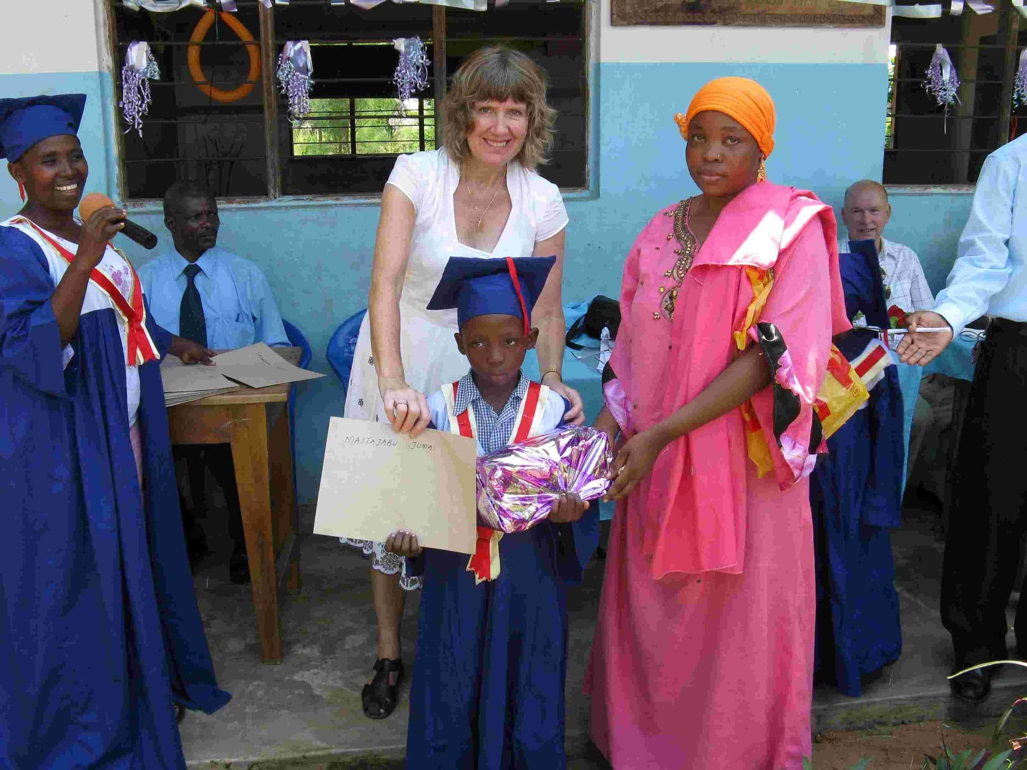 A young graduate in a blue gown holding a certificate and present between two women