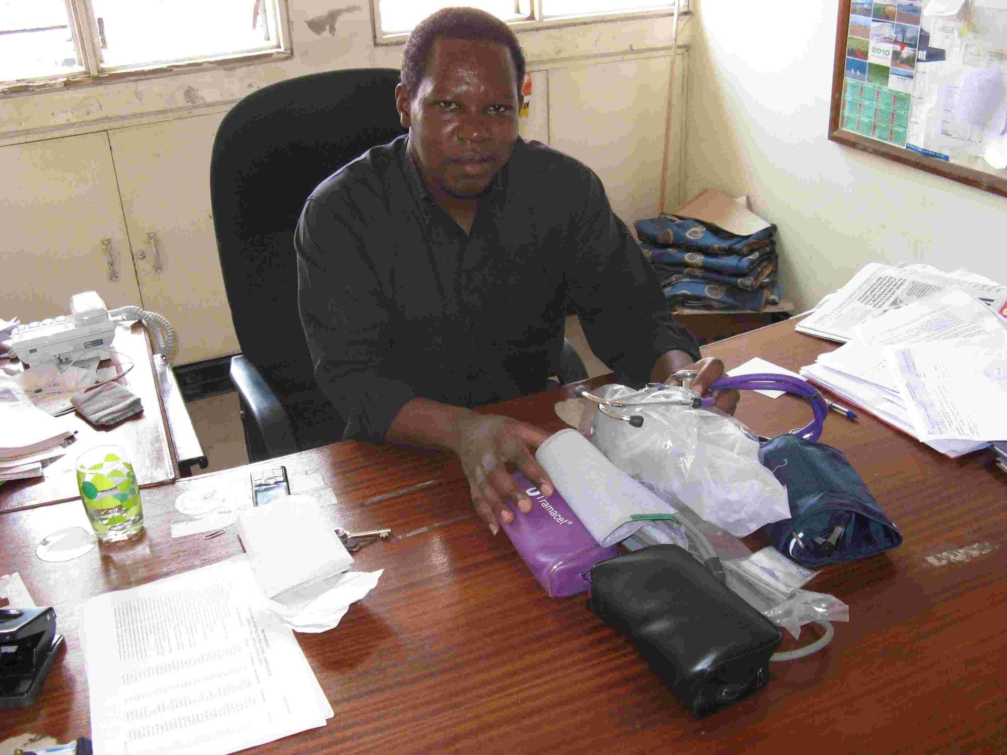 A doctor at his desk with donated blood pressure monitors and medical supplies