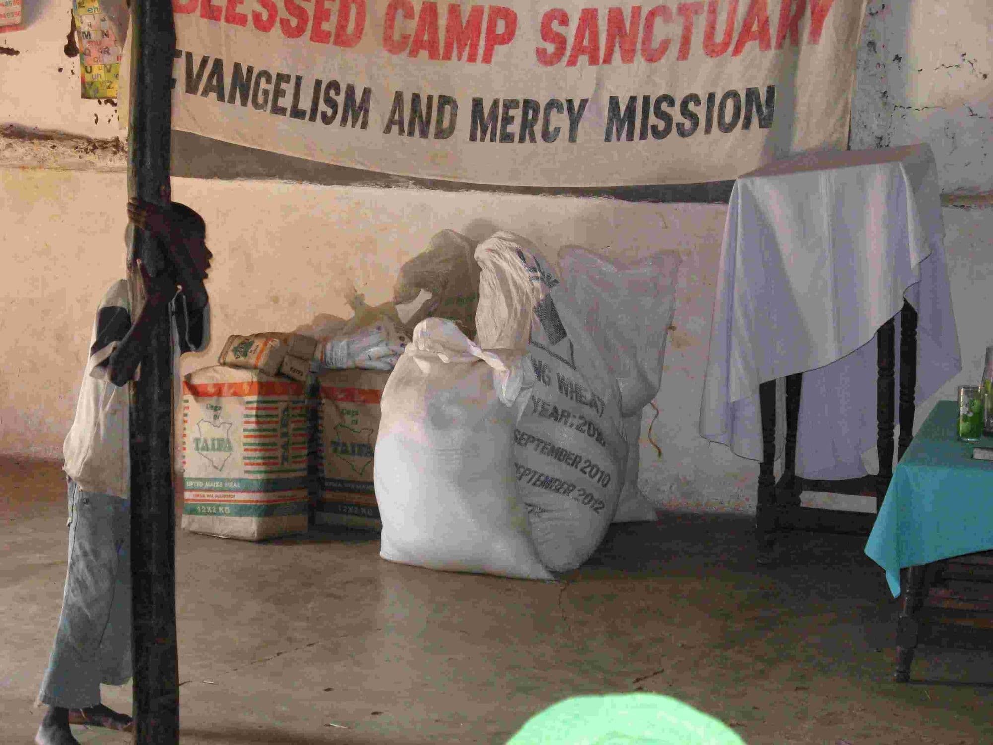 Sacks of food stacked under a Blessed Camp Sanctuary Evangelism and Mercy Mission banner