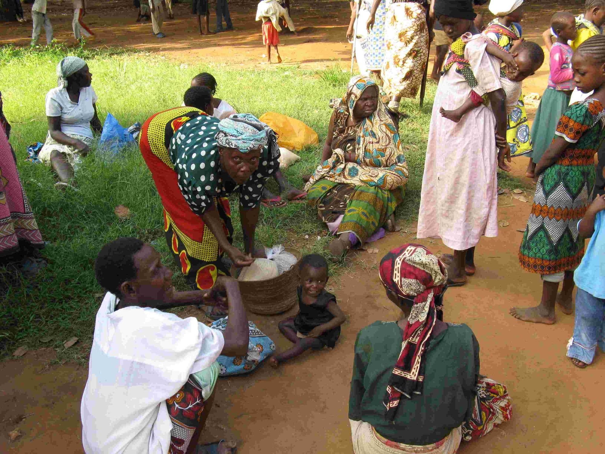 Women dividing out sacks of maize flour on the ground at a food distribution