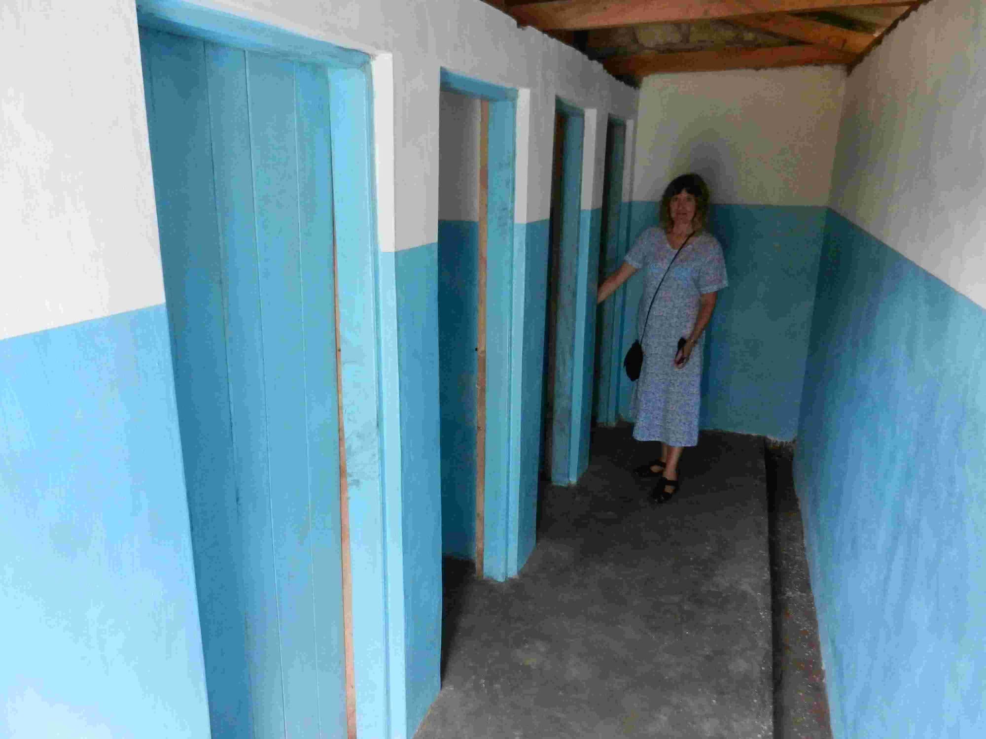 Blue-painted cubicles inside a new toilet block with a visitor in the doorway